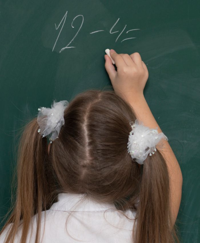 Young girl writing a subtraction problem on a chalkboard during class.