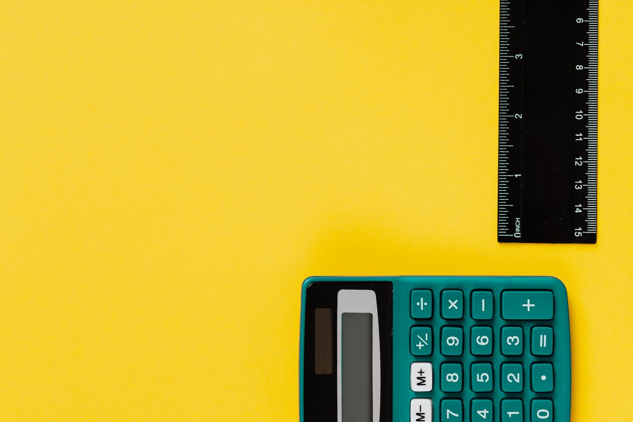 A bright teal calculator and black ruler on a vivid yellow surface. Ideal for educational themes.