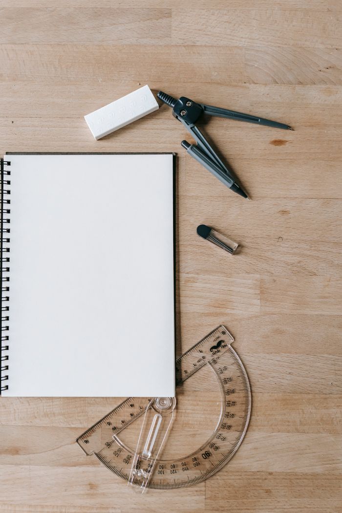 Top view of blank notebook and protractor near compass and eraser on wooden desk