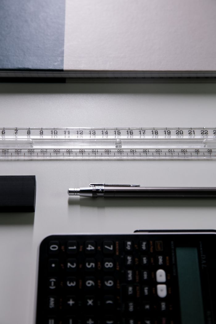 A flat lay of office supplies including a calculator, ruler, and pen on a white desk.